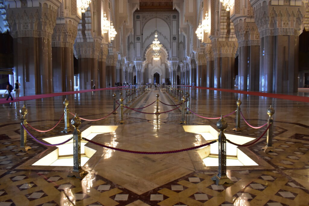 Interno della moschea Hassan II, con file di colonne decorate, lampadari e riflessi sul pavimento lucido.