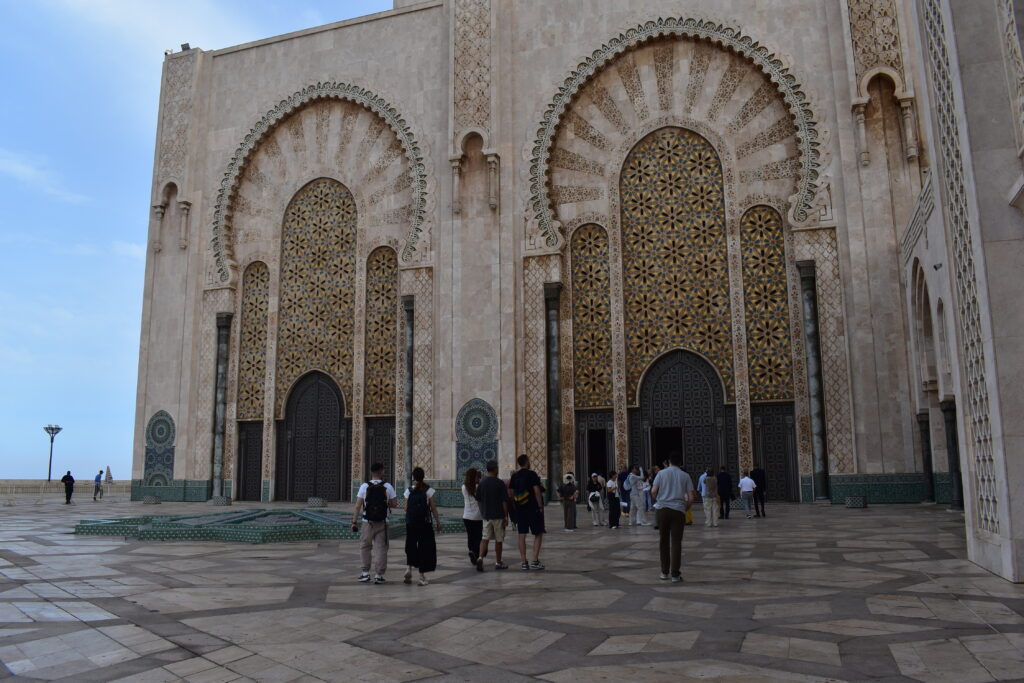 Viaggio in Marocco. Visitatori davanti alle grandi porte della moschea Hassan II, incorniciate da archi e decorazioni geometriche.